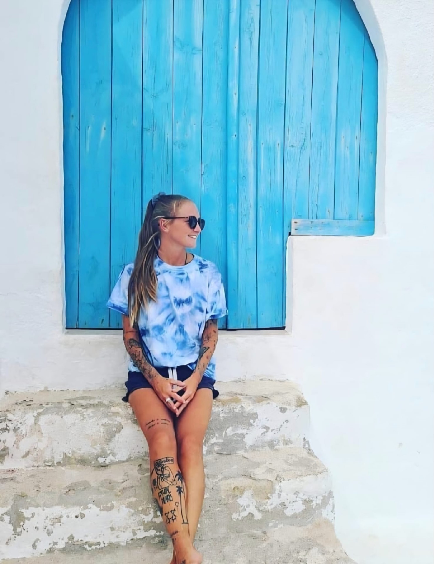 Beth sitting in front of a bright blue Mediterranean door